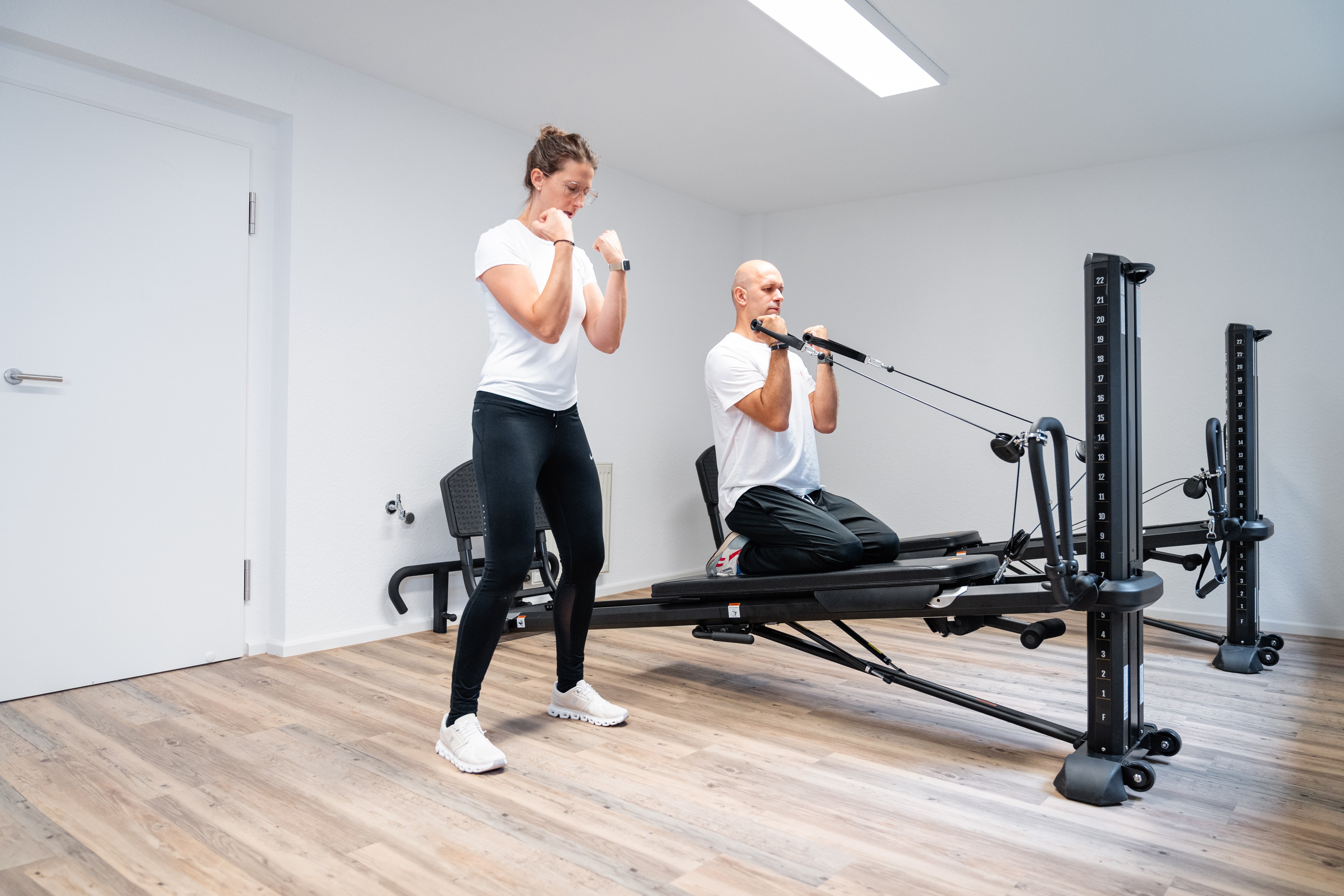Patient beim aktivem Training am Total Gym Gerät mit Physiotherapeut zur Stärkung der Oberkörpermuskulatur bei Inphynity Physio in Köln-Flittard